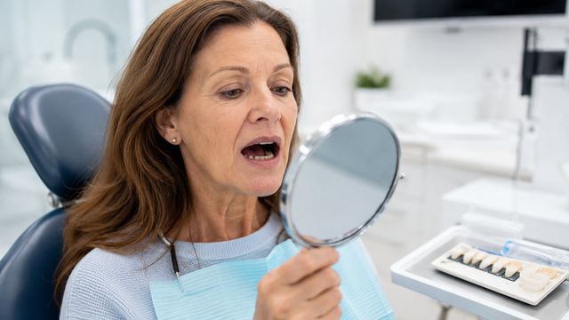 Paciente sorrindo ao espelho em consultório odontológico em Barueri após avaliação de gengiva saudável